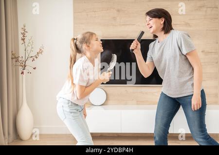 Famiglia felice madre giovane adulta e figlia adolescente carina che si diverte a cantare karaoke con i pennelli. madre ridendo godendo Foto Stock