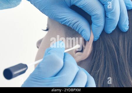 Controllo dell'orecchio con batuffolo di cotone in laboratorio medico, tonalità blu Foto Stock