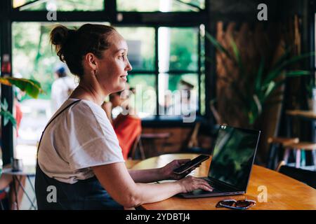 Donna simpatica e ispirata che lavora in remoto da un accogliente bar su un computer portatile utilizzando le tecnologie wireless. Foto Stock