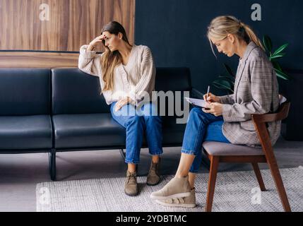 Una donna sconvolto in una crisi emotiva seduta su un divano e un consulente psicoterapista in ufficio. Foto Stock