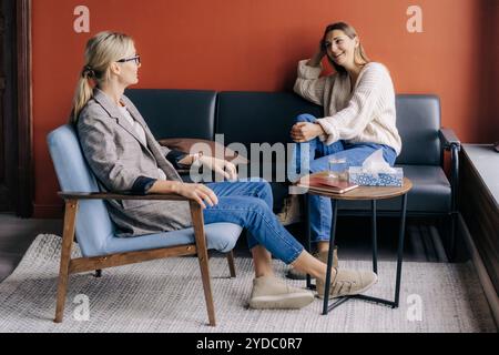 Giovane donna rilassata che parla con il terapista in un ufficio accogliente. Piacevole conversazione tra due donne Foto Stock