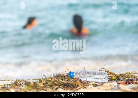 Immagine ravvicinata di una bottiglia d'acqua di plastica vuota su una spiaggia sporca piena di alghe, rifiuti e rifiuti su una spiaggia sabbiosa sporca con buco Foto Stock