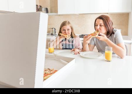 Madre e figlia seduta in cucina e mangiare la pizza e divertirsi. Focus sulla figlia Foto Stock