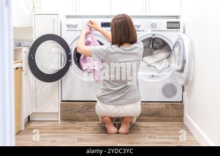 Donna che carica vestiti sporchi in lavatrice per lavare nella moderna stanza degli accessori Foto Stock