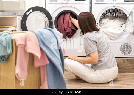 Donna che carica vestiti sporchi in lavatrice per lavare nella moderna stanza degli accessori Foto Stock