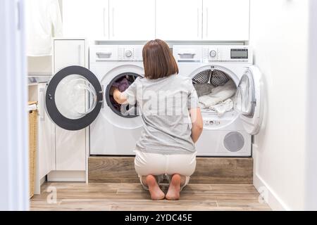 Donna di mettere i vestiti per macchina di lavaggio per lavare Foto Stock