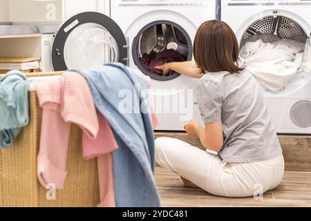 Donna che carica vestiti sporchi in lavatrice per lavare nella moderna stanza degli accessori Foto Stock