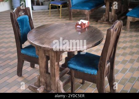 Tavolo rustico in legno con due sedie con cuscini in velluto blu in un ambiente da caffe'. Disposizione interna dei posti a sedere per la cena. Ristorante informale e hospita Foto Stock