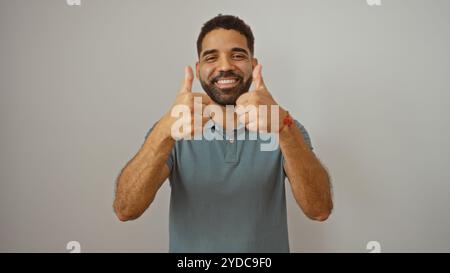 Giovane che regala i pollici su sfondo bianco isolato, sorride e guarda la fotocamera Foto Stock