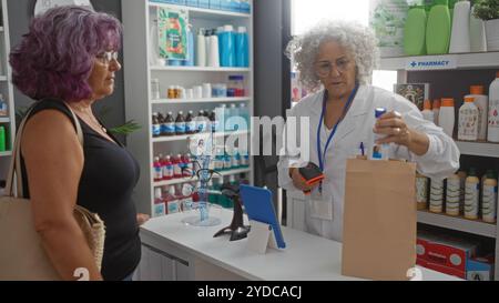 Farmacista donna anziana che assiste un cliente donna matura nell'interno della farmacia con farmaci sugli scaffali Foto Stock