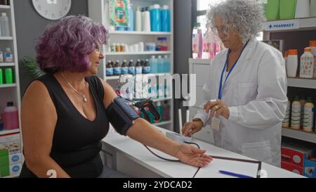 Donna che riceve la pressione sanguigna controllata da una farmacista donna all'interno di una farmacia con scaffali pieni di farmaci e prodotti Foto Stock
