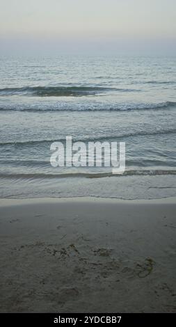 Il tranquillo paesaggio della spiaggia, che mostra dolci onde che incontrano la spiaggia di sabbia sotto un cielo calmo al crepuscolo, crea un'atmosfera tranquilla sul mare Foto Stock