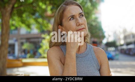 Donna bionda matura che pensa all'aperto nel parco urbano durante il giorno Foto Stock