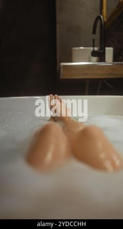 Una giovane donna si rilassa in un bagno di bolle in un lussuoso hotel, mostrando le sue gambe in un ambiente sereno. Foto Stock