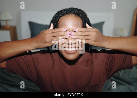 Donna sorridente che copre gli occhi con le mani in casa Foto Stock