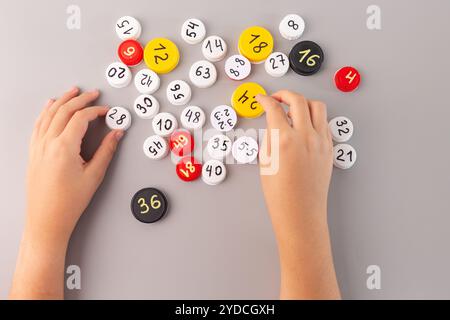 Mani dei bambini sistemando tappi per bottiglie di plastica con numeri e dati moltiplicati su sfondo grigio attività didattica di matematica per i bambini che imparano e.. Foto Stock