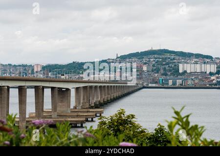 Dundee Scozia: 4 agosto 2024: Il Tay Bridge si estende su un calmo corpo d'acqua con un cielo nuvoloso sopra in un paesaggio urbano Foto Stock