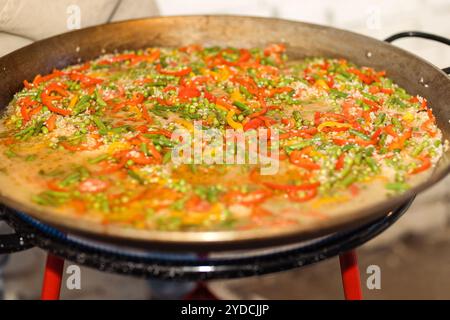 Cuocere la paella in una padella grande in metallo. Un tradizionale piatto spagnolo con riso e verdure. Piselli, peperoni e fiocchi di riso sono cotti Foto Stock