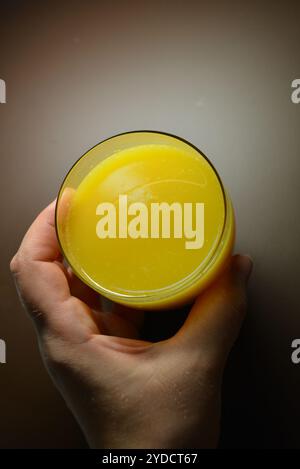 Foto bellissime e insolite di prodotti alimentari. Succo di frutta multicolore giallo brillante, arancione, arancione e versato in un piccolo bicchiere trasparente. Foto Stock