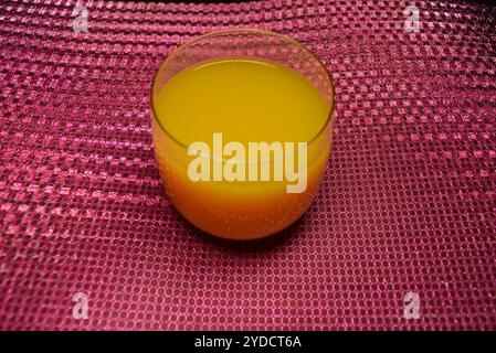 Foto bellissime e insolite di prodotti alimentari. Succo di frutta multicolore giallo brillante, arancione, arancione e versato in un piccolo bicchiere trasparente. Foto Stock