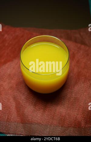Foto bellissime e insolite di prodotti alimentari. Succo di frutta multicolore giallo brillante, arancione, arancione e versato in un piccolo bicchiere trasparente. Foto Stock