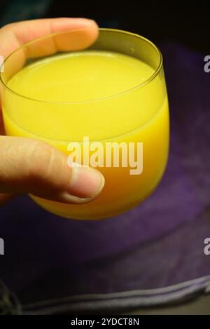 Foto bellissime e insolite di prodotti alimentari. Succo di frutta multicolore giallo brillante, arancione, arancione e versato in un piccolo bicchiere trasparente. Foto Stock