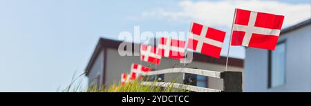 Bandiere bianche su rosse danesi in fila su una recinzione di legno nel villaggio scandinavo durante le festività nazionali. Formato banner largo lungo con blu Foto Stock