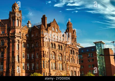 Un alto e ornato edificio in mattoni con torri e torrette multiple, circondato da un cielo blu con nuvole bianche. L'edificio ha molte finestre, intricate Foto Stock