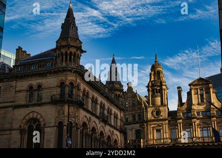 Un'immagine a basso angolo di diversi edifici in pietra ornati con guglie e dettagli intricati su un cielo blu luminoso con nuvole bianche a Manchester, Regno Unito. Foto Stock