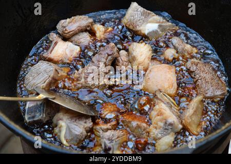 Il processo di cottura del pilaf uzbeko. La carne di manzo viene fritta nell'olio in un calderone di ghisa. Cucina tradizionale uzbeka orientale, pilaf o plov con pezzi grandi Foto Stock