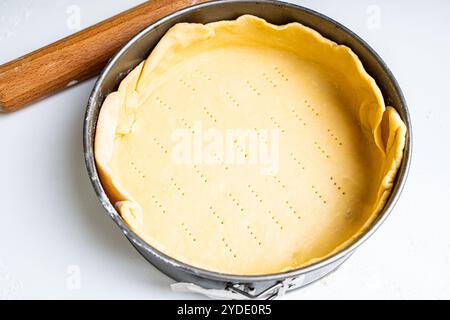 Impastare in un piatto da forno su un tavolo bianco e un mattarello. Ricetta di Quiche loren. Foto di alta qualità Foto Stock