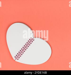 Creative vista superiore piana dei laici a forma di cuore ad notepad con pagine vuote come mockup con copia spazio sulla coral colore sfondo carta stile minimal. Modello Foto Stock