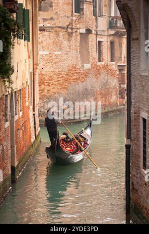 Una gondola con turisti che scendono lungo un piccolo canale fiancheggiato da case urbane Foto Stock