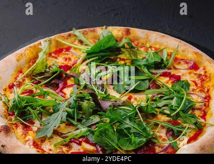 Pizza con rucola su tavola nera Foto Stock