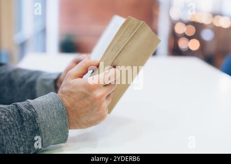 Giovane uomo che legge il vecchio libro di carta aperto al tavolo, primo piano, stile vintage Foto Stock