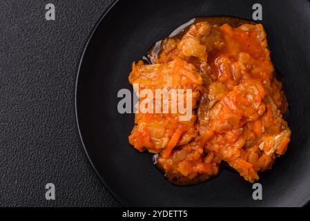 Affettare il pesce in salsa di pomodoro con sale e spezie su uno sfondo di cemento scuro Foto Stock