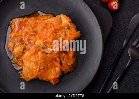 Affettare il pesce in salsa di pomodoro con sale e spezie su uno sfondo di cemento scuro Foto Stock