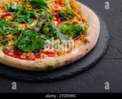 Pizza con rucola su tavola nera Foto Stock