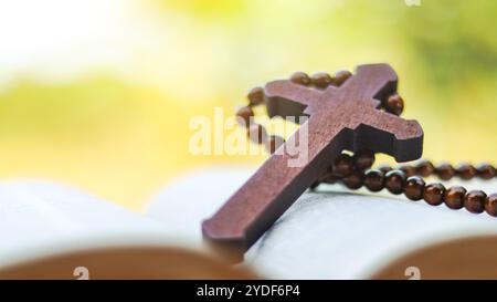 Croce di legno rosso scuro appoggiata su un vecchio libro aperto che simboleggia la diffusione dell'amore di Gesù Cristo tra i cristiani, che riflette la fede la devozione e il Foto Stock