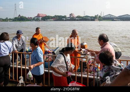 Thailandia. 25 ottobre 2024. I monaci che stanno in piedi su una barca sono visti ricevere elemosine dalla gente, sulla riva del fiume Chao Phraya al tempio Wat Chin Wararam Worawihan, nella provincia di Pathum Thani, Thailandia. La tradizione di dare l'elemosina a un centinaio di monaci a Pathum Thani, Thailandia, è una cerimonia buddista secolare che si svolge lungo fiumi e canali dopo la fine della Quaresima buddista. I monaci si riuniscono in barca per ricevere offerte dalla gente del posto, che prepara il cibo e partecipa alla preparazione del merito. Questo evento celebra la comunità, la fede e il patrimonio culturale. Credito: SOPA Images Limited/Alamy Live News Foto Stock