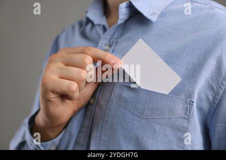 Uomo che prende un biglietto da visita vuoto dalla tasca della giacca su sfondo grigio, primo piano. Mockup per il design Foto Stock