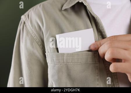 Uomo che prende un biglietto da visita vuoto dalla tasca della giacca su sfondo verde, primo piano. Mockup per il design Foto Stock