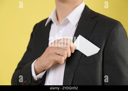 Uomo che prende un biglietto da visita vuoto dalla tasca della giacca su sfondo giallo, primo piano. Mockup per il design Foto Stock