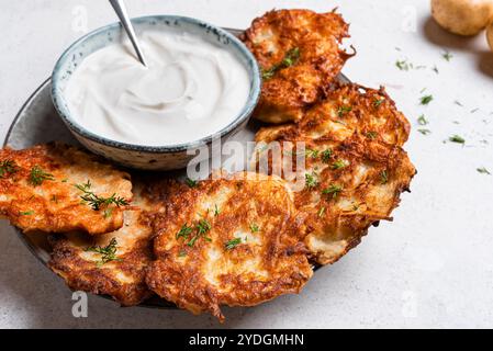 Latkes di patate fatte in casa con panna acida sul piatto da vicino. Latke o levivot ebraiche tradizionali. Hash Brown. Foto Stock