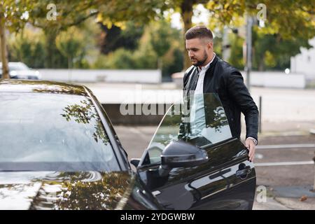 Il bel tipo barbuto apre una porta della sua auto di lusso nel parcheggio. L'uomo finisce il lavoro e torna a casa Foto Stock