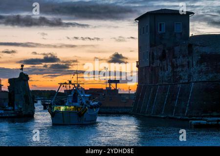 Barca che esce da Darsena Vecchia a Livorno al tramonto, con la sagoma degli edifici storici e il porto sullo sfondo, l'Italia Foto Stock