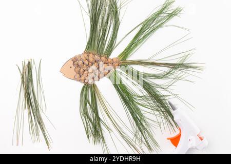 cartone tagliato a forma di pesce, con piccole scaglie di pino incollate su di esso. Le alette e la coda sono realizzate con aghi di pino, pistola per colla a caldo, vista dall'alto, wh Foto Stock