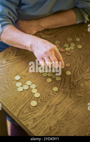 donna anziana seduta miseramente a tavola a casa e a contare le monete. Foto di alta qualità Foto Stock