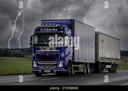 Veicolo per il trasporto merci Volvo FH blu personalizzato in movimento durante la tempesta estiva. Filtraggio artistico, solo per uso editoriale. Luopajarvi, Finlandia. Foto Stock