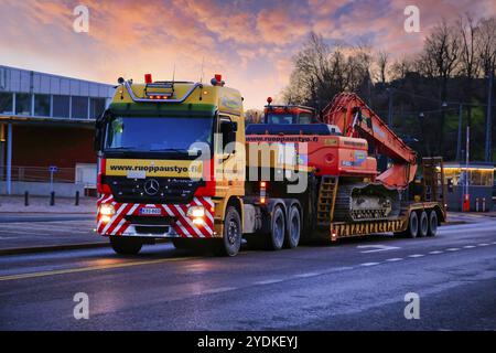 Rimorchio per autocarro Mercedes-Benz Actros con caricatore basso Ruoppaustyo trasporta l'escavatore Doosan DX 300 LC al tramonto. Helsinki, Finlandia. 19 dicembre 2019 Foto Stock